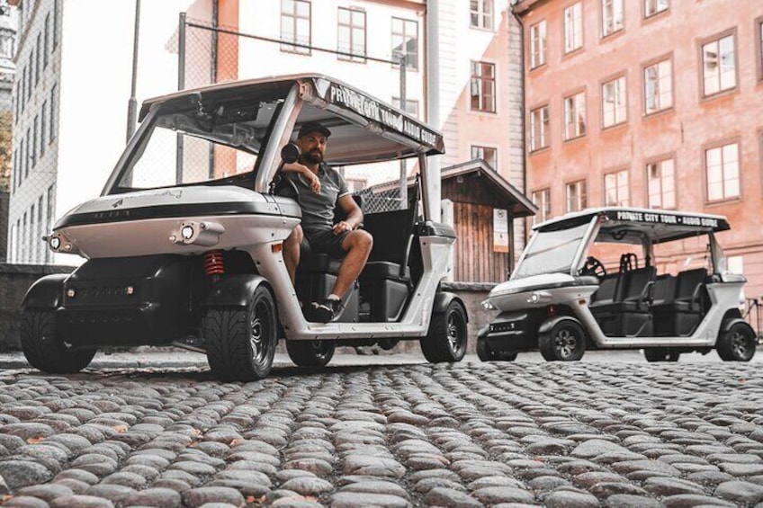 Two golf carts parked on cobblestone pavement in an urban setting. 2