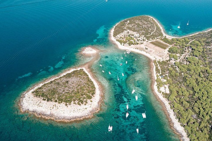 An aerial view of a coastal area with clear blue waters, two small islands with sandy beaches, and boats anchored near the shore. 2