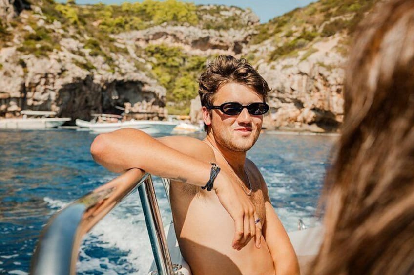 A person on a boat with rocky cliffs and clear blue water in the background. 2