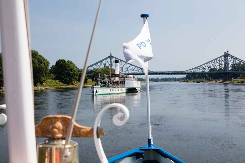 A boat with a white flag marked "PD" on a river, with a bridge in the background. 1