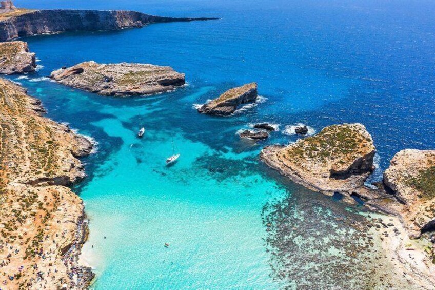 A coastal landscape with clear turquoise waters, rocky outcrops, and a sandy beach. 5
