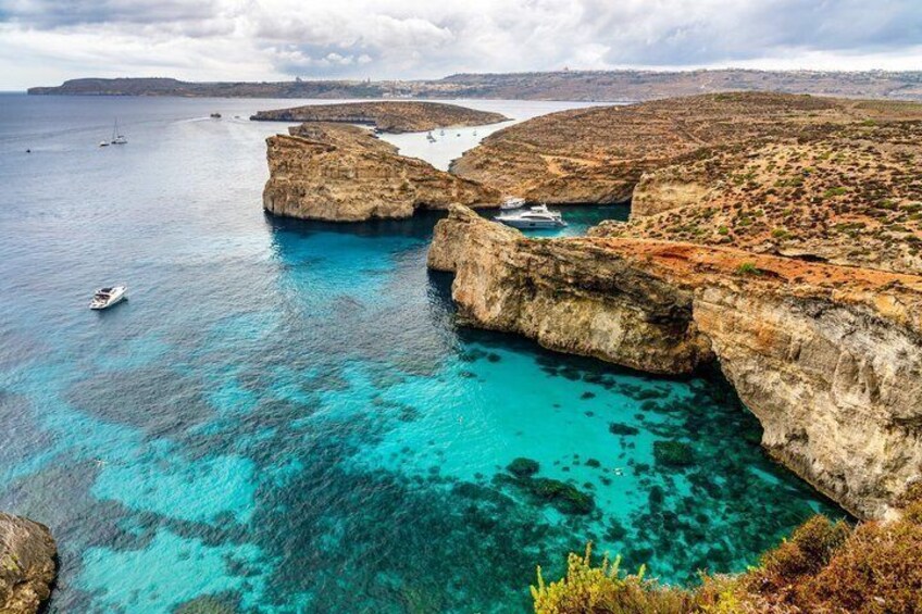 A coastal landscape with clear turquoise waters, rocky cliffs, and boats. 4