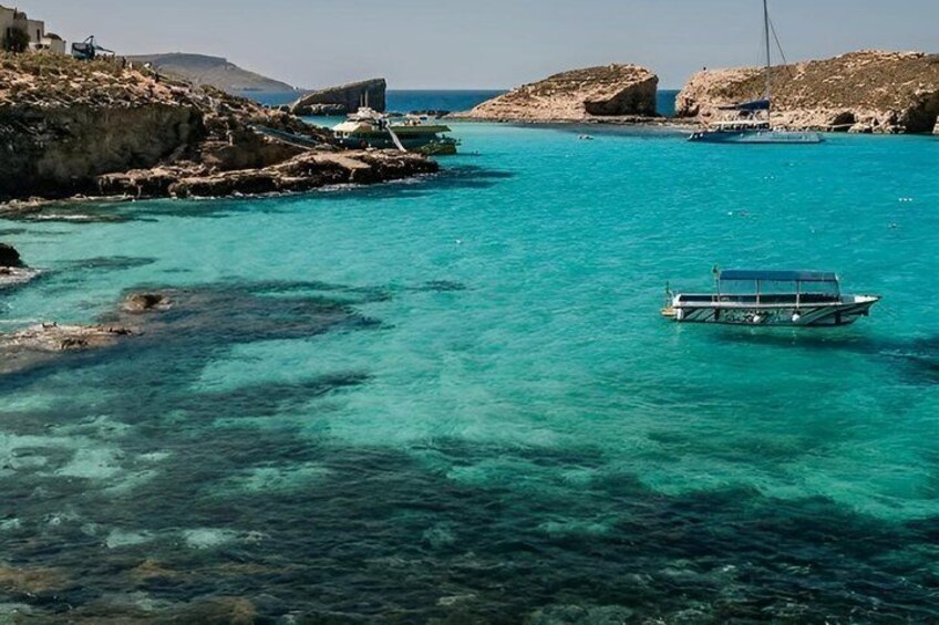 A boat on turquoise water, rocky coastline, and distant buildings. 3