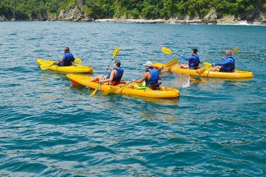 Four people kayaking on a calm body of water with a rocky shoreline in the background. 1
