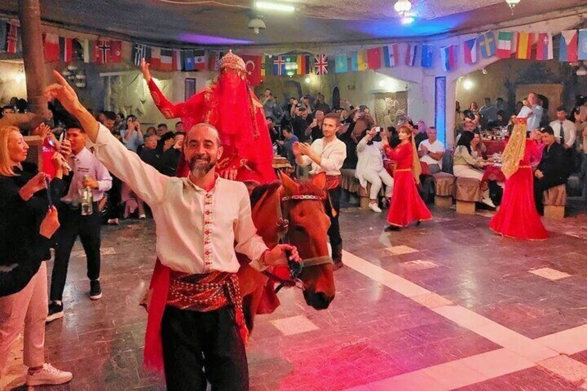 Un homme, vêtu d’un costume traditionnel, danse avec un cheval dans un décor festif à l’intérieur. 5