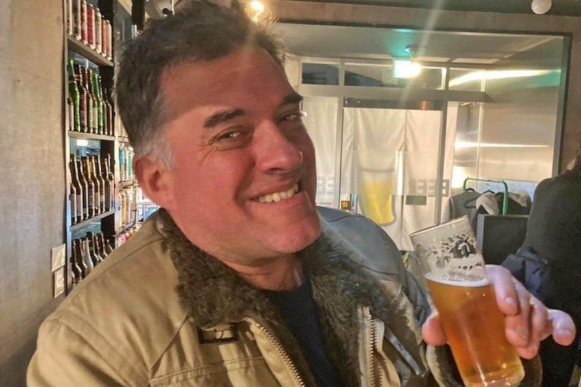 Una persona sostiene una jarra de cerveza en un bar, con estantes llenos de botellas al fondo. 2