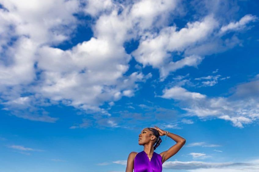 Una persona con remera morada de pie frente a un cielo azul con nubes. 3