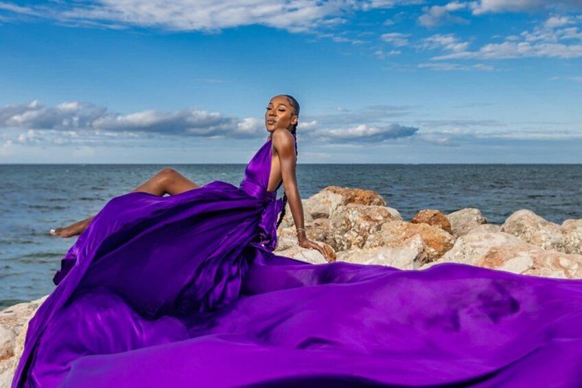 Una persona con un vestido morado sentada sobre rocas junto al mar. 4