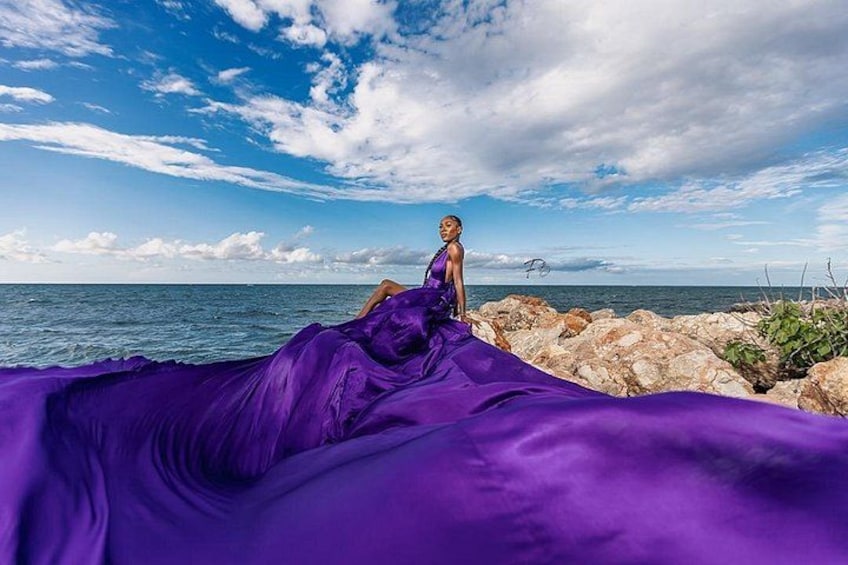 Una persona con un vestido morado sentada sobre rocas junto al mar. 5