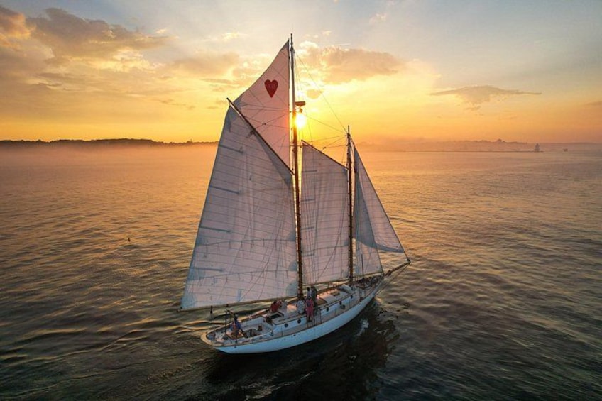 A sailboat with a heart symbol on its sail, sailing on calm waters during sunset. 1