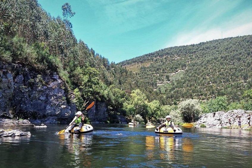 Two kayakers on a calm river surrounded by forested hills. 3