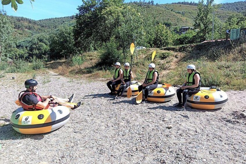 People sitting on inflatable rafts on a gravel path with trees and hills in the background. 1