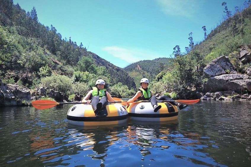Two people in inflatable rafts on a calm river surrounded by greenery and rocks. 2