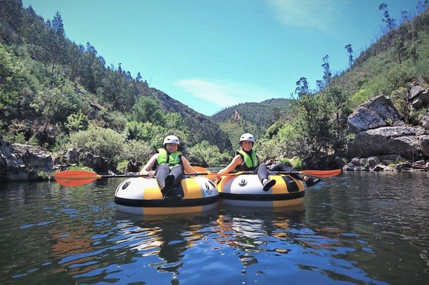Two people in inflatable rafts on a calm river surrounded by greenery and rocks. 2