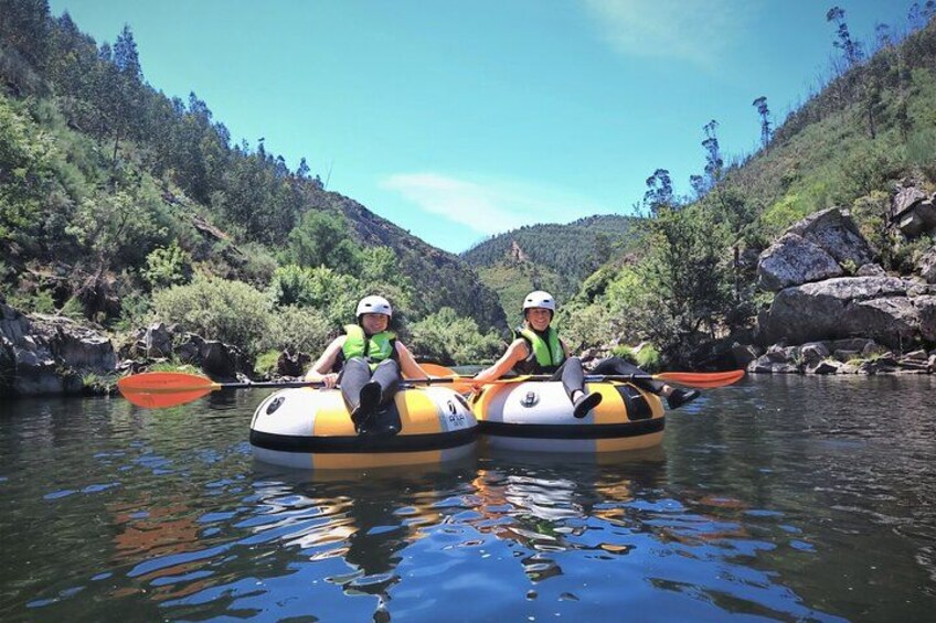 Dos personas en una balsa inflable amarilla y negra sobre un río rodeado de follaje y rocas. 2