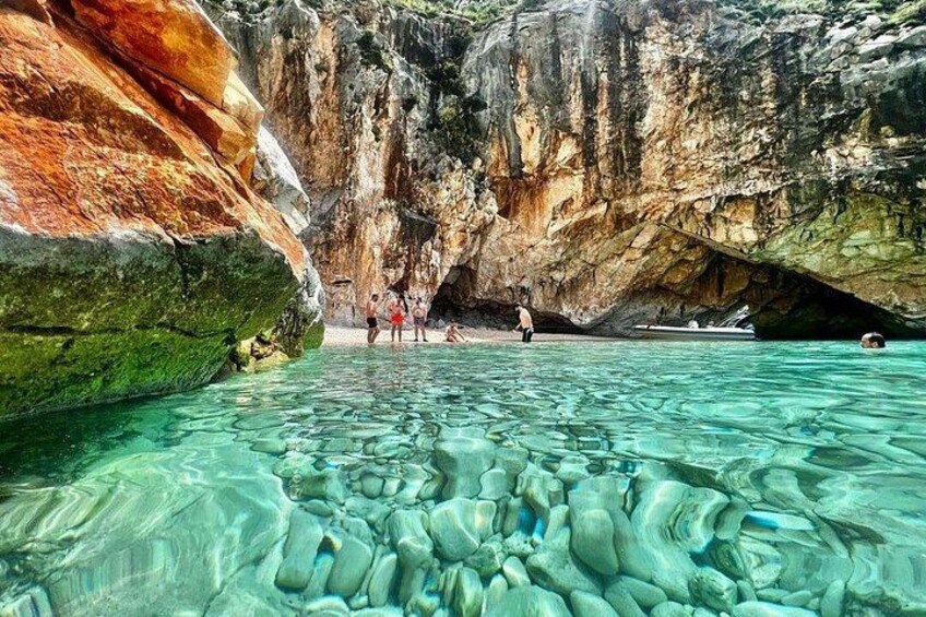 Une piscine d’eau cristalline, entourée de falaises rocheuses et bordée par l’entrée d’une grotte. 1