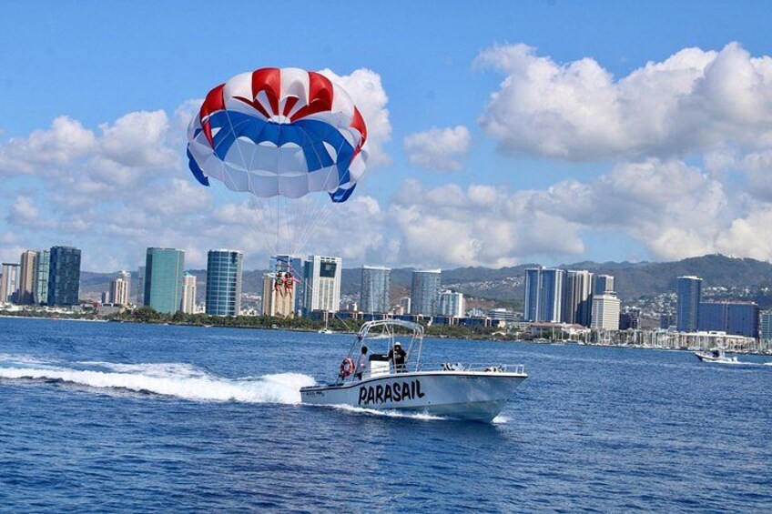 En båd til parasailing med en faldskærm i luften, en bysilhuet i baggrunden og en klar blå himmel. 2
