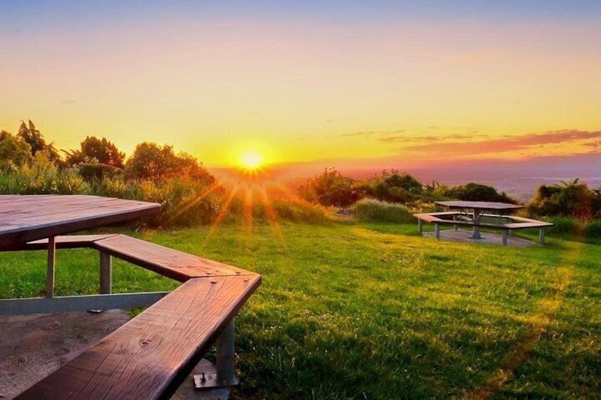 A sunset over a grassy field with picnic tables. 2