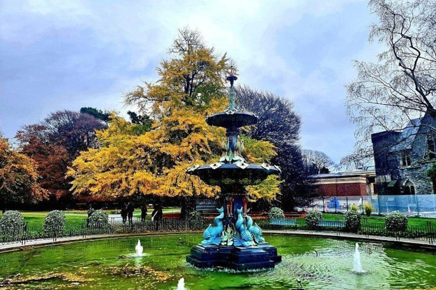 A fountain with a statue, surrounded by a well-maintained garden with trees and a building in the background. 5