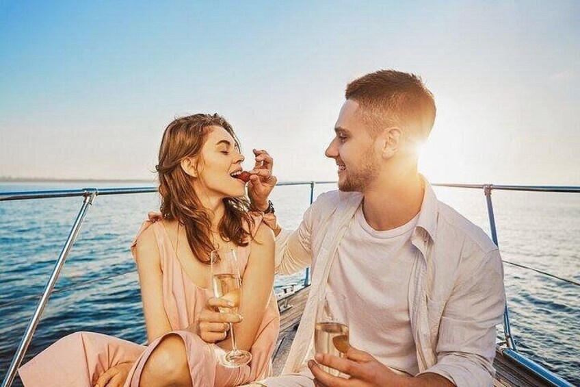 Dos personas sentadas en un bote con bebidas, una barandilla y agua al fondo. 1