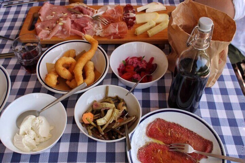 A table with various food items including cheese, cured meats, pickled vegetables, and a bottle of sauce. 1