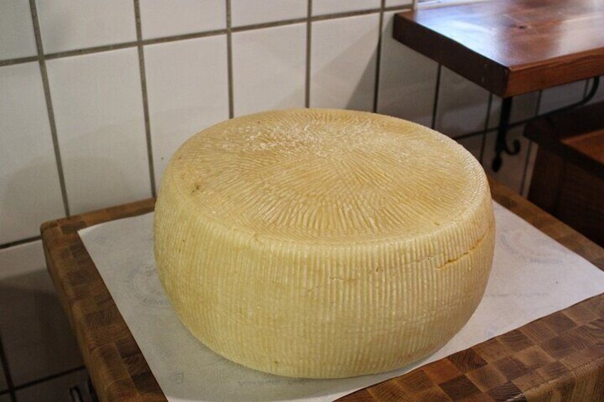 A large wheel of cheese on a wooden cutting board in a kitchen. 4