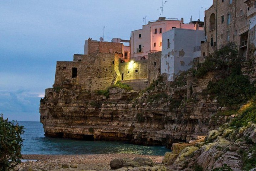 A coastal cliff with buildings, a rocky shoreline, and a body of water. 3