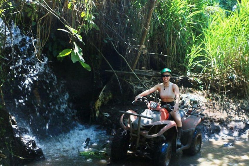 A person riding an ATV through a forested area with a stream. 5