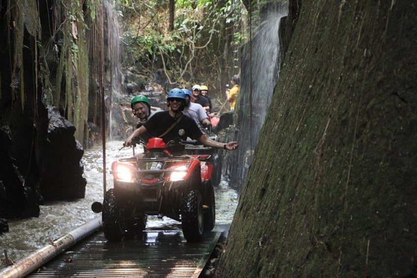 People riding ATVs through a narrow, rocky waterway surrounded by trees. 2
