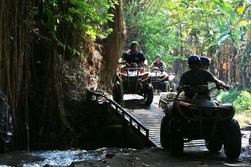 People riding ATVs on a wooden bridge in a forested area. 4