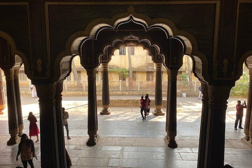 An architectural structure with arches and columns, a paved courtyard, and people walking. 3
