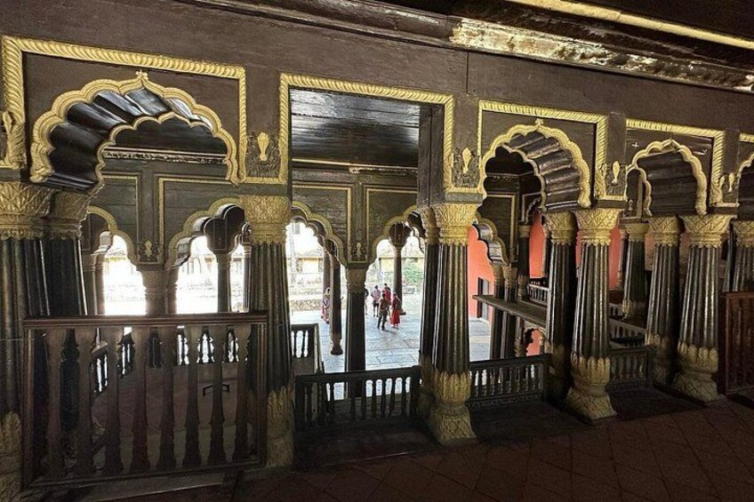 An interior with ornate arches and columns, a tiled floor, and a view of an outdoor area with people. 3