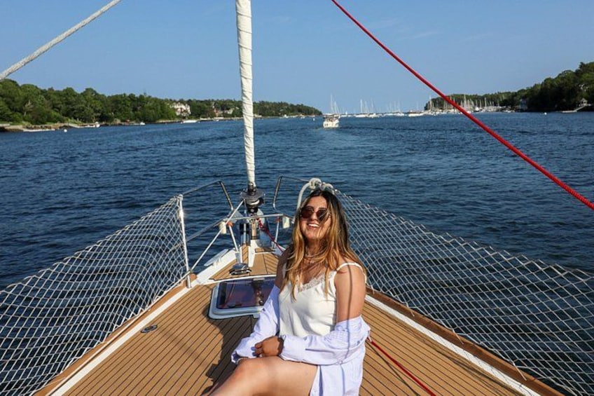 A person on a sailboat with a view of a river and distant buildings. 5