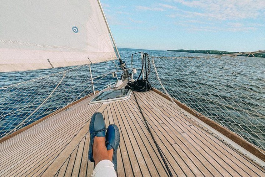 A wooden deck on a sailboat with a person sitting and a sail in the background. 2