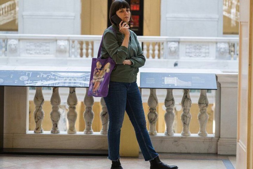 A person standing on a balcony with a railing, holding a phone and a purple bag. 4