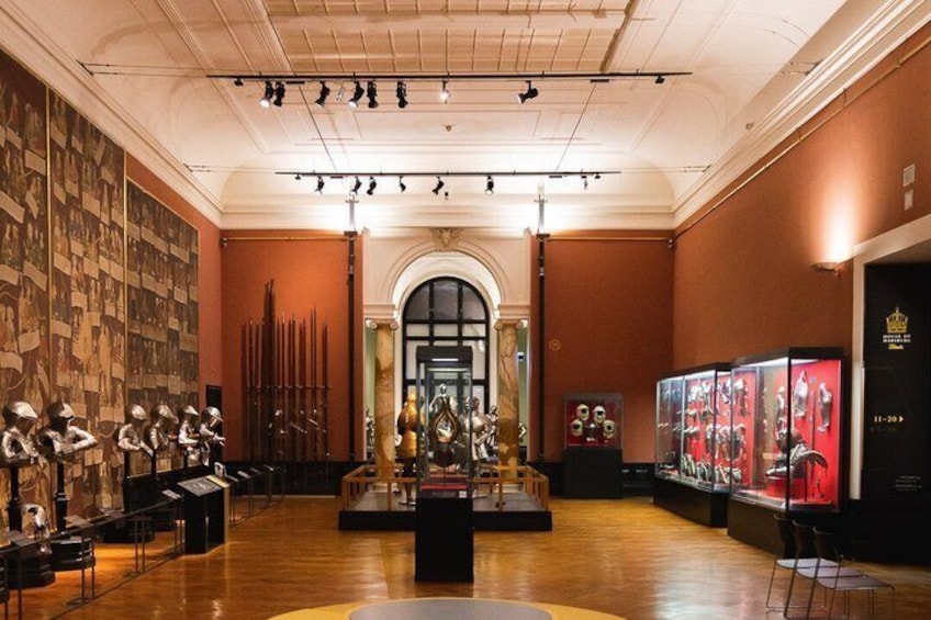 A museum interior with classical statues, a central altar, and a display of armor. 2