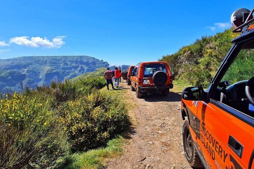 A dirt path with orange vehicles and people hiking in a mountainous area. 1