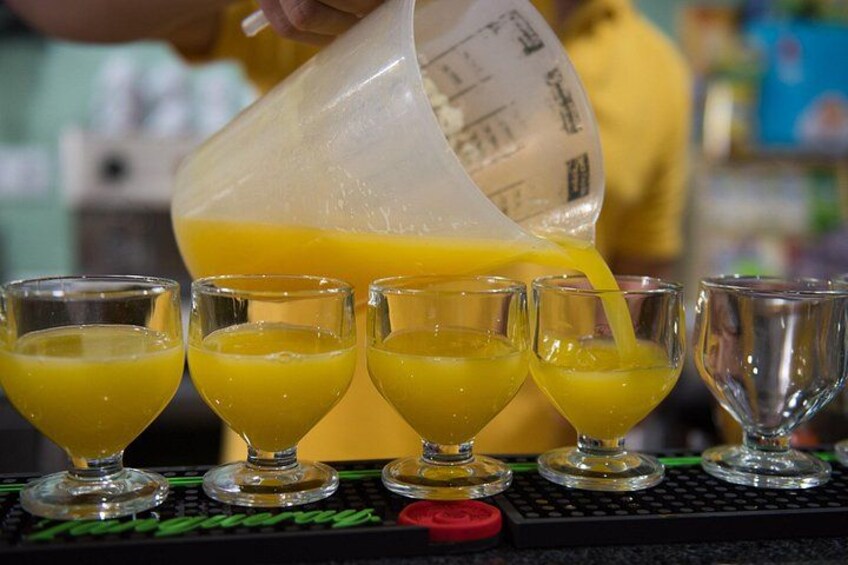 A person pouring orange juice into shot glasses on a bar counter. 3