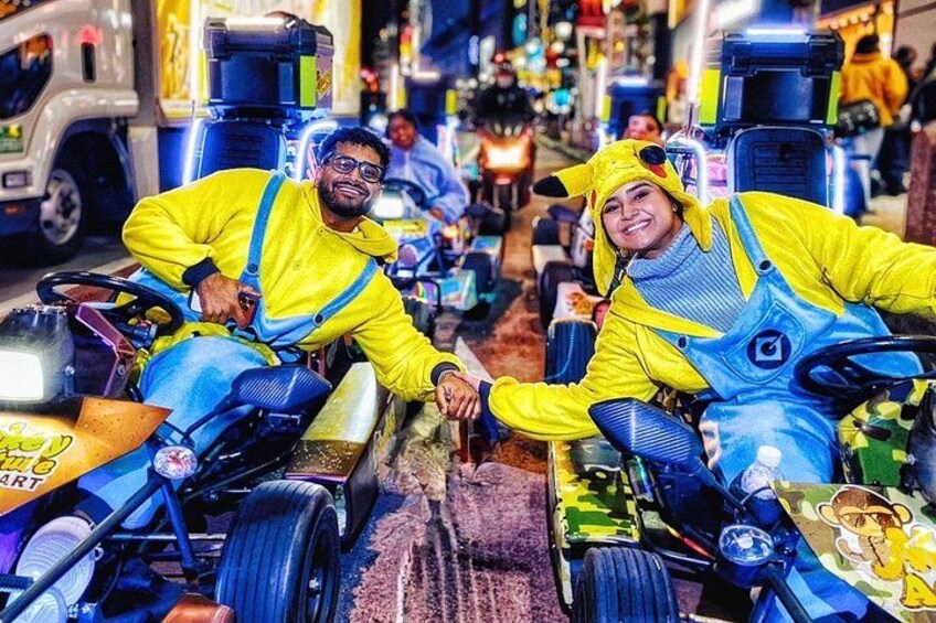 Two people in yellow and blue overalls on tricycles in a busy indoor setting. 2