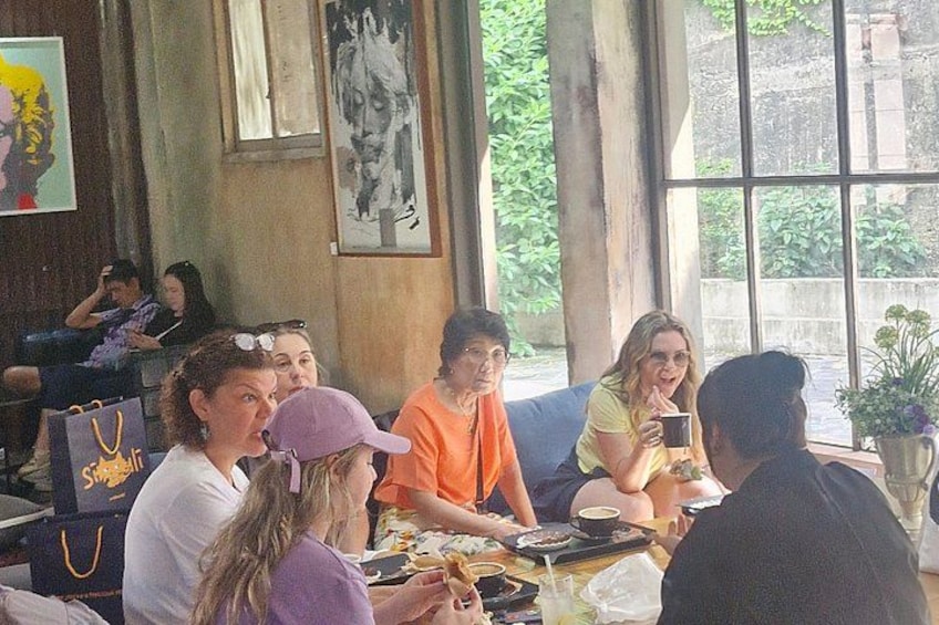 Eine Gruppe von Personen sitzt an einem Tisch in einem Café mit großen Fenstern und Kunstwerken an den Wänden. 2