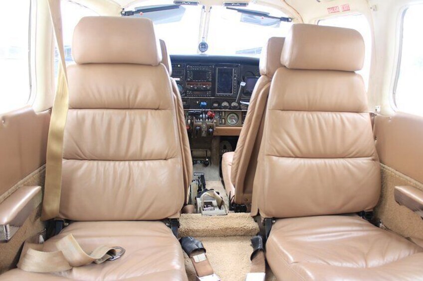 The interior of a small aircraft with two beige leather seats, a control panel, and a small storage compartment. 2