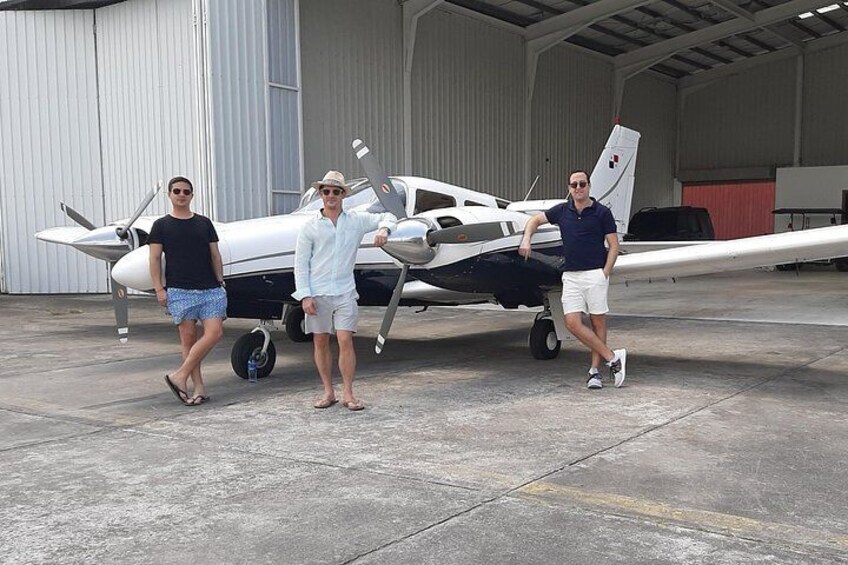 Three people standing in front of a small white and blue airplane in a hangar. 1