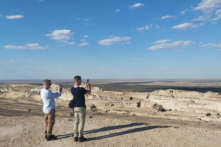 Deux personnes prennent une photo d’un paysage désertique caractérisé par des formations rocheuses en strates. 4