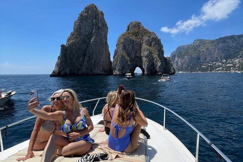 A boat with three people taking a selfie, rocky cliffs in the background, and calm water. 4