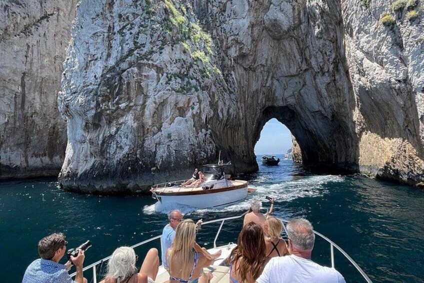 A boat passing through a natural rock arch in a body of water. 3