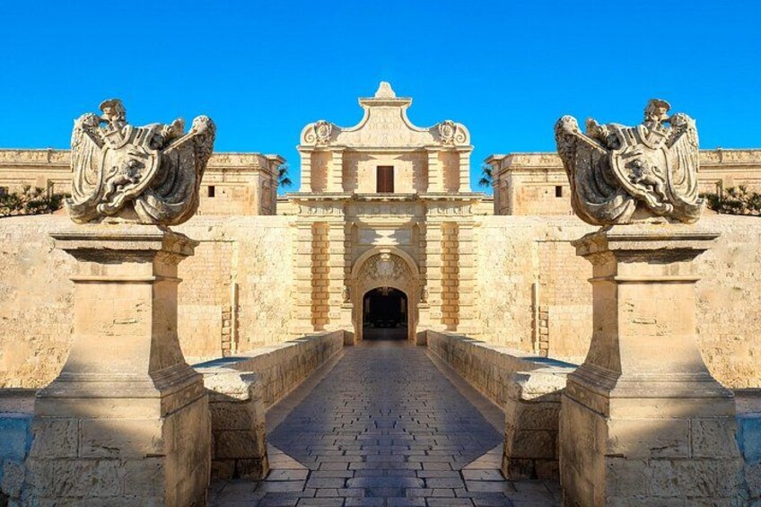 A historical stone archway leading to a building with a central entrance and statues on either side. 2