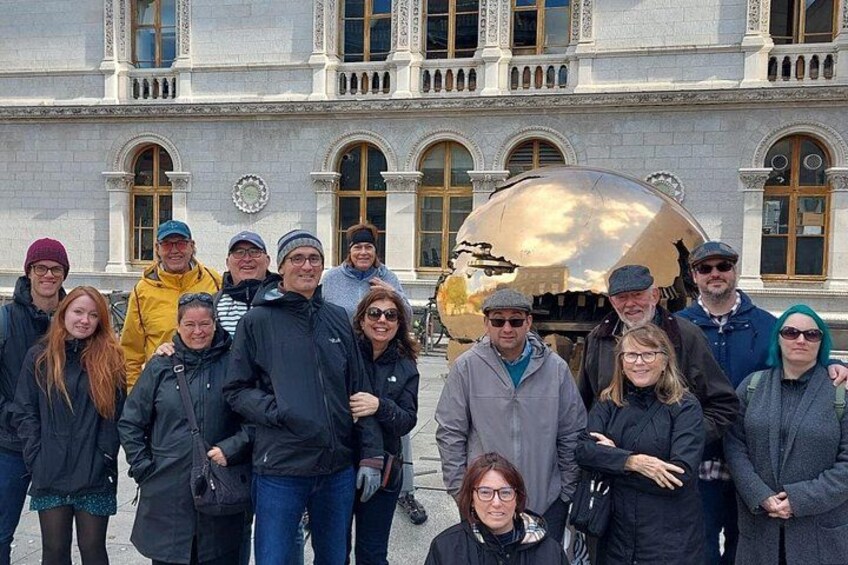 Un groupe de personnes se tient devant un bâtiment doté de fenêtres en arc de cercle et d’une grande sculpture dorée. 2