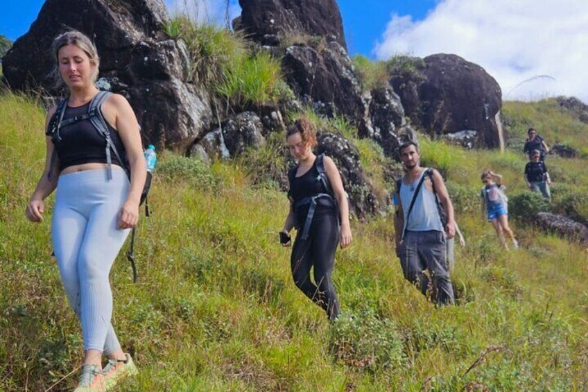 A group of hikers on a grassy trail with rocky outcrops in the background. 3