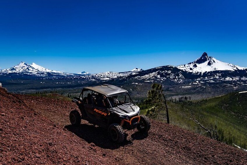 A 4x4 vehicle on a dirt path with snow-capped mountains in the background. 2