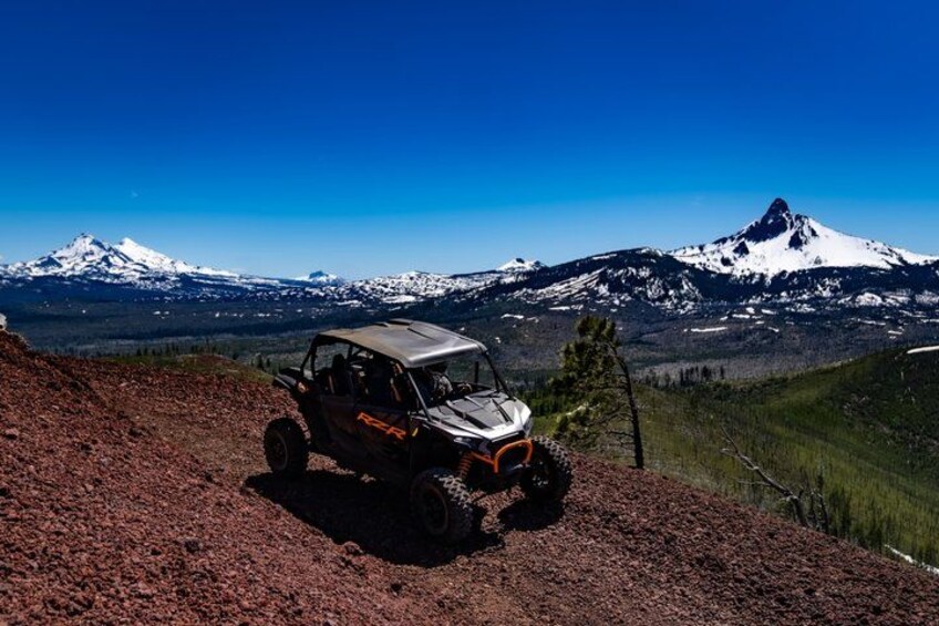 A vehicle on a dirt path with snow-capped mountains in the background. 4